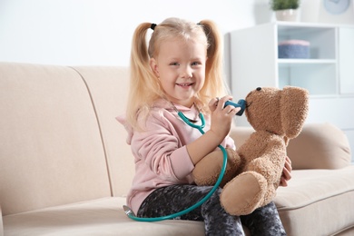 Cute child imagining herself as doctor while playing with toy bunny on couch at home