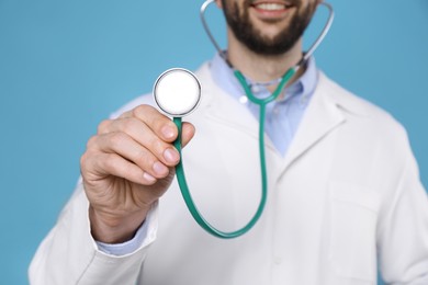 Doctor with stethoscope on light blue background, closeup. Cardiology concept