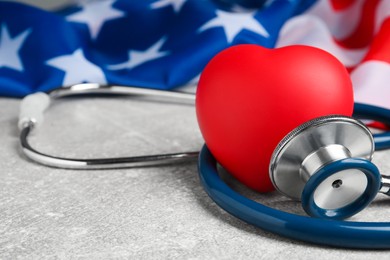 Red heart, stethoscope and American flag on light grey table, closeup. Space for text