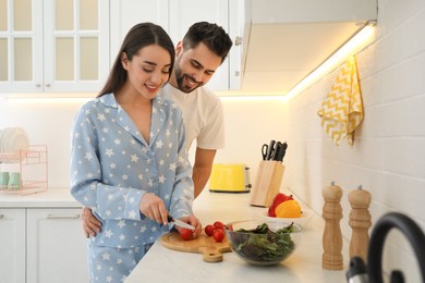 Happy couple in pajamas cooking at kitchen counter
