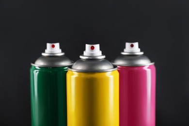 Photo of Colorful cans of spray paints on black background, closeup