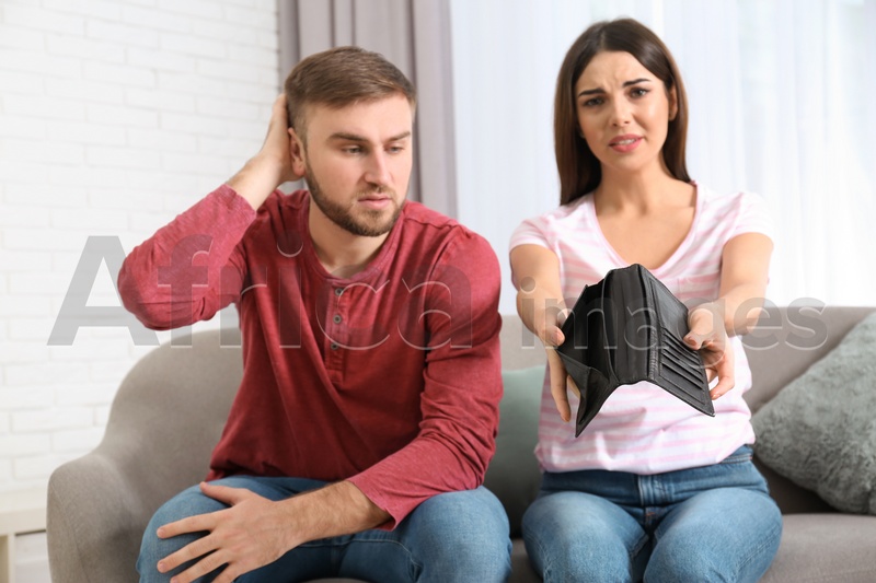 Unhappy young couple with empty wallet at home. Money problems
