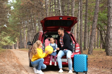 Young family with suitcases and car in forest