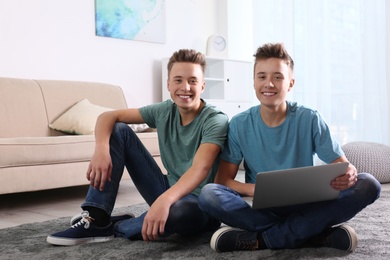 Teenage twin brothers using laptop together in living room