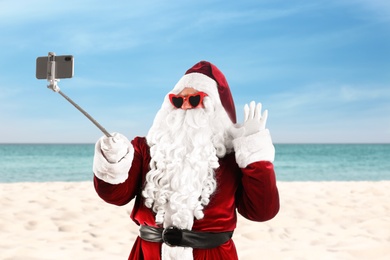 Santa Claus in sunglasses taking selfie on beach near sea. Christmas vacation 