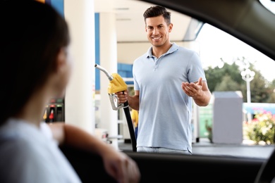 Man with fuel pump nozzle talking to his girlfriend at self service gas station