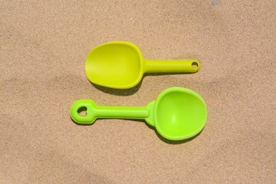 Photo of Colorful plastic shovels on sand, flat lay. Beach toys