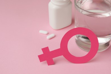 Female gender sign, pills and glass of water on pink background, closeup. Space for text