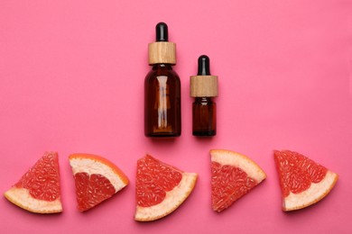 Bottles of citrus essential oil and fresh grapefruit slices on pink background, flat lay