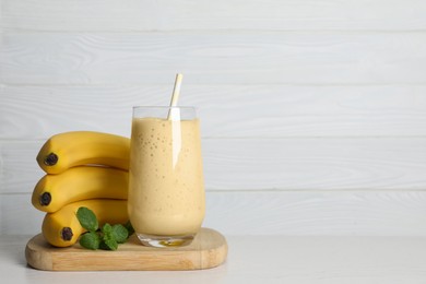 Glass of tasty smoothie, mint and fresh bananas on white wooden table. Space for text