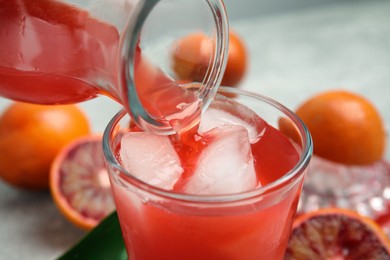 Pouring tasty sicilian orange juice into glass, closeup