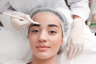 Young woman getting prepared for procedure of permanent eyebrow makeup in tattoo salon