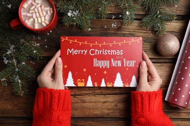 Photo of Woman holding greeting card at wooden table, top view. Christmas celebration