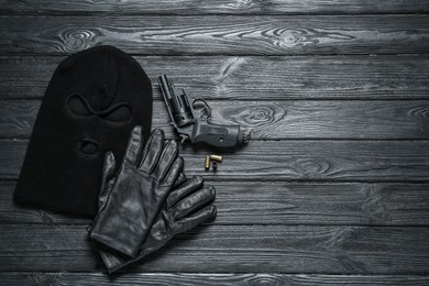 Photo of Black knitted balaclava, gloves and gun on grey wooden table, flat lay. Space for text
