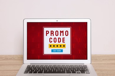 Photo of Laptop with activated promo code on wooden table near white wall