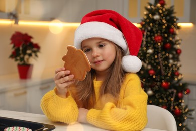 Cute little girl with Christmas gingerbread cookie at table indoors