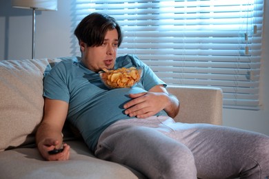 Overweight man with chips watching TV on sofa at home