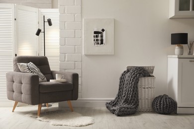 Photo of Living room interior with armchair, pouf and chunky knit blanket