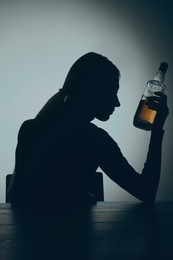 Alcohol addiction. Silhouette of woman with bottle of whiskey at wooden table, backlit