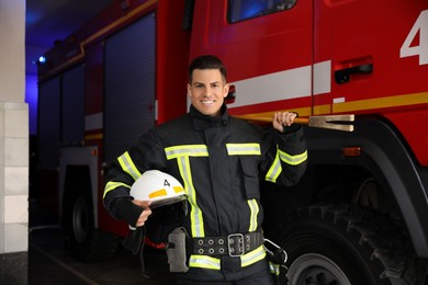 Portrait of firefighter in uniform with helmet and entry tool near fire truck at station