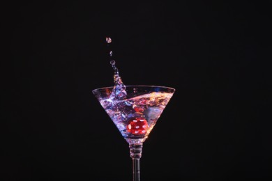 Casino dice falling into glass of alcohol drink on black background