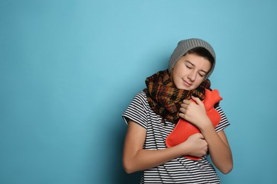 Sick teenage boy with hot water bottle on turquoise background. Space for text