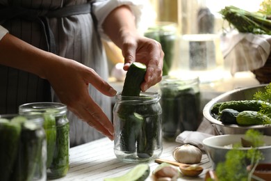 Photo of Woman putting cucumbers into jar in kitchen, closeup. Canning vegetables