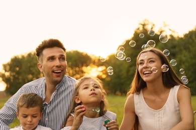 Happy family blowing soap bubbles in park at sunset. Summer picnic