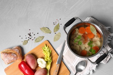 Pot of delicious vegetable bouillon and ingredients on light grey table, flat lay