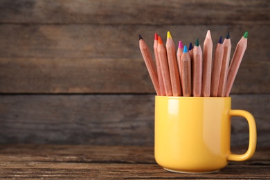 Colorful pencils in cup on wooden table. Space for text