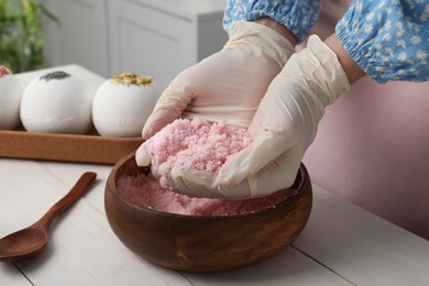 Woman in gloves making bath bomb mixture at white table indoors, closeup