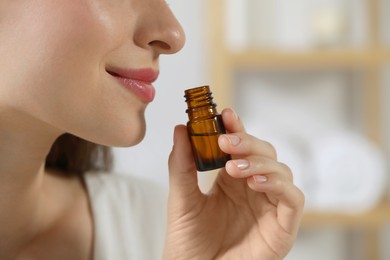 Photo of Young woman smelling essential oil on blurred background, closeup. Space for text