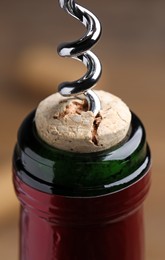 Photo of Opening wine bottle with corkscrew on blurred background, closeup