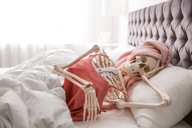 Human skeleton in silk pajamas and towel lying on bed indoors