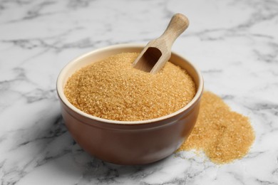 Brown sugar and scoop in bowl on white marble table, closeup