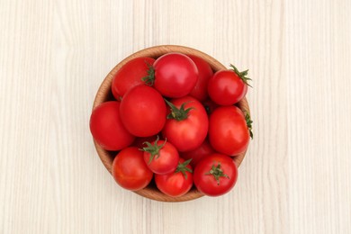 Bowl of ripe red tomatoes on light wooden table, top view