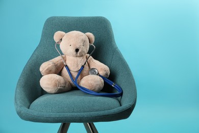 Teddy bear with stethoscope in armchair on light blue background, space for text. Pediatrician practice