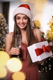 Beautiful woman in Santa hat with Christmas gift and champagne at home