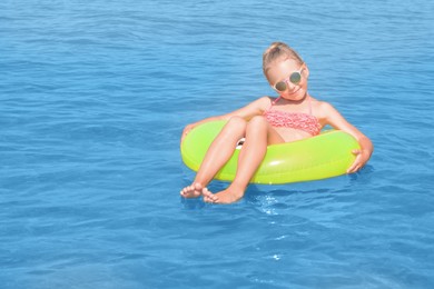 Happy little girl with inflatable ring in sea on sunny day, space for text