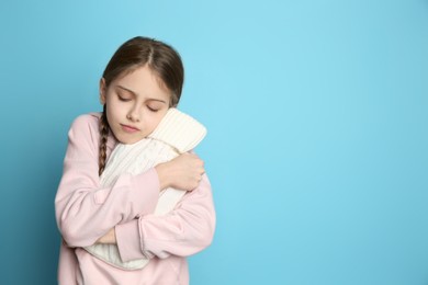 Photo of Ill girl with hot water bottle suffering from cold on light blue background, space for text
