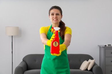 Woman showing bottle of toxic household chemical with warning sign indoors