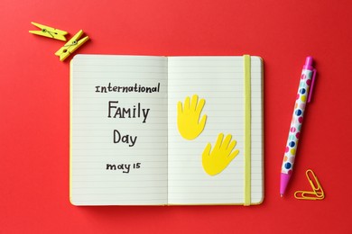 Notebook with text International Family Day May 15 and stationery on red background, flat lay