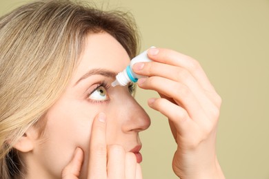 Young woman using eye drops on pale olive background, closeup