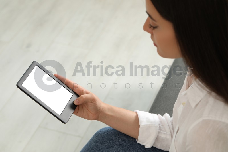 Young woman using e-book reader indoors, closeup