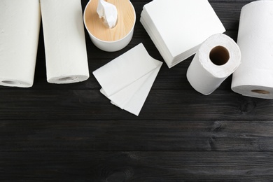 Clean napkins, box with tissues and rolls of paper towels on wooden table, flat lay. Space for text