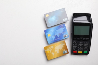 Modern payment terminal and credit cards on white table, flat lay. Space for text
