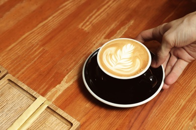 Barista putting cup of coffee on wooden table, closeup. Space for text