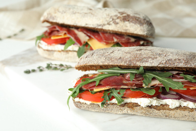 Photo of Delicious sandwiches with fresh vegetables and prosciutto on white table, closeup