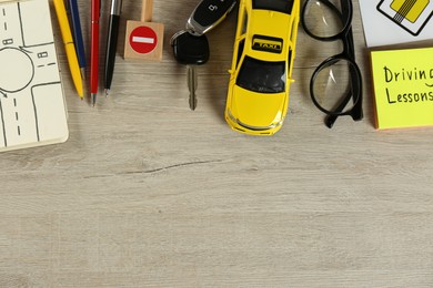 Flat lay composition with driving lessons workbook and toy car on wooden background, space for text. Passing license exam