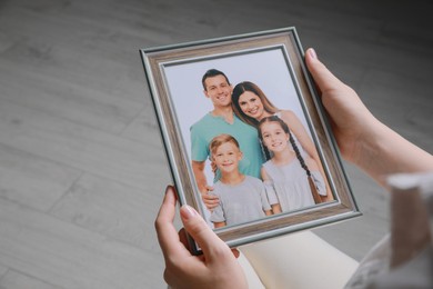 Woman holding framed family photo indoors, closeup